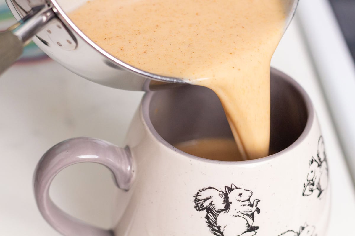 Pumpkin Spice Chai Latte | thewendthousekitchen.com Pouring pumpkin chai latte into a coffee cup with squirrels on it.