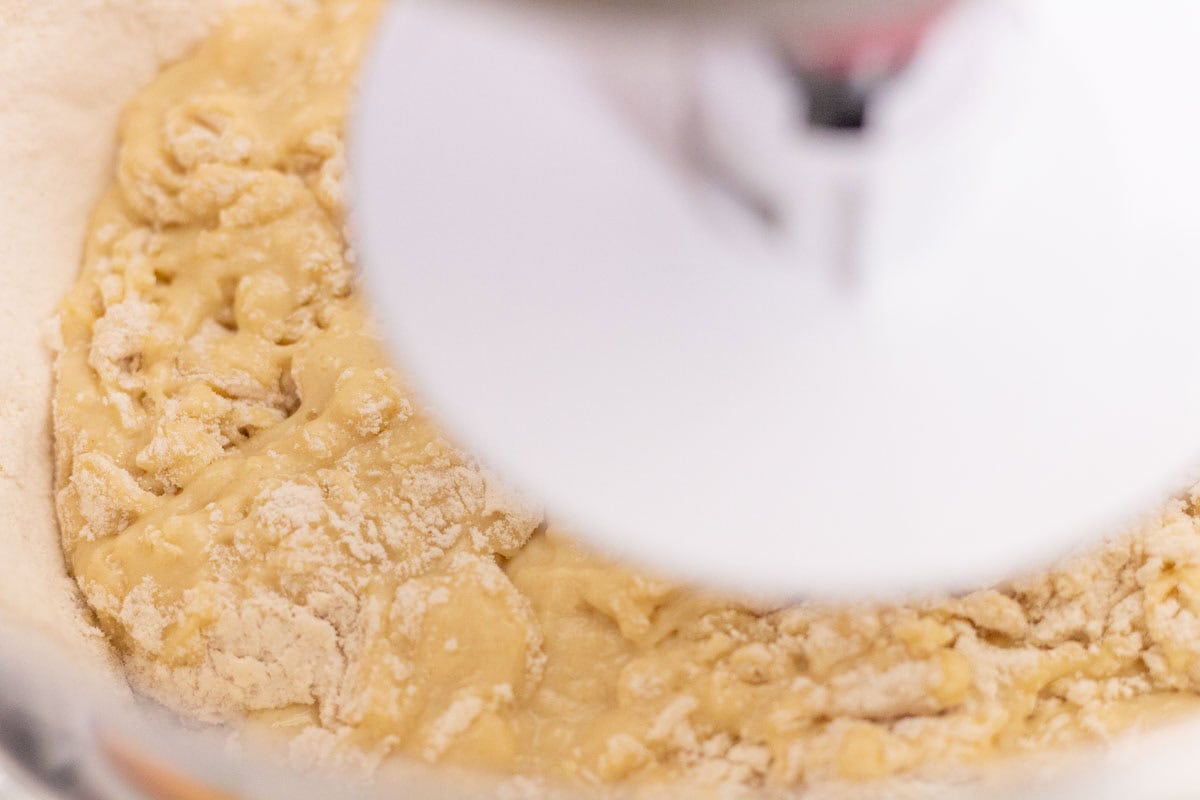 Sour Dough Discard Cinnamon Rolls | thewendthousekitchen.com Mixing flour into cinnamon roll ingredients in the bowl of a stand mixer.