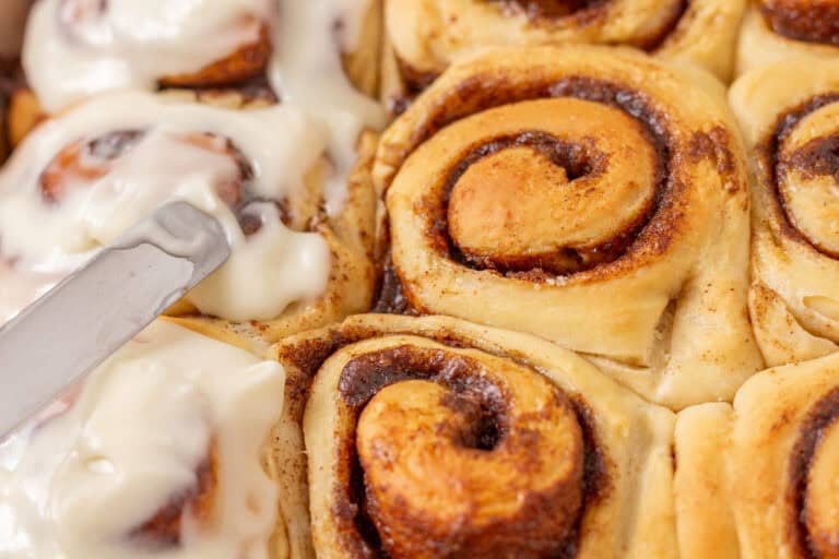 Icing Sour dough discard cinnamon rolls in a pan.