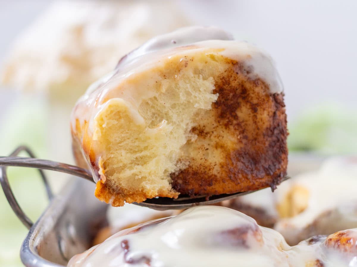 Lifting a cinnamon bun out of the pan with a fork.