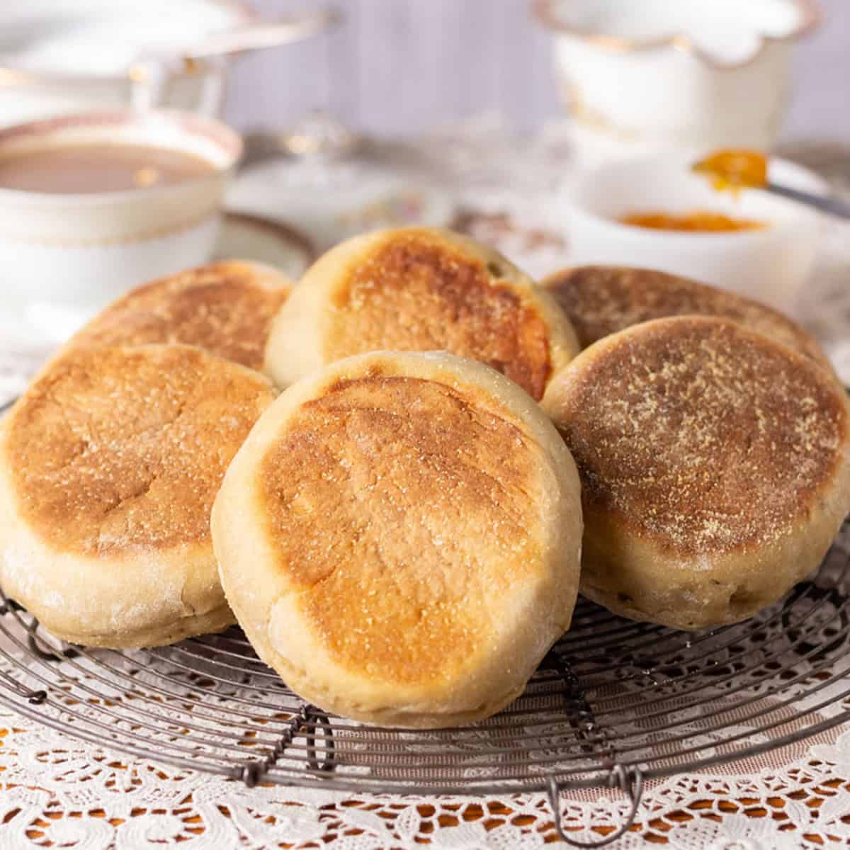 Sourdough discard English muffins on a black wire round cooling grid with a cup of coffee and jam in the background.