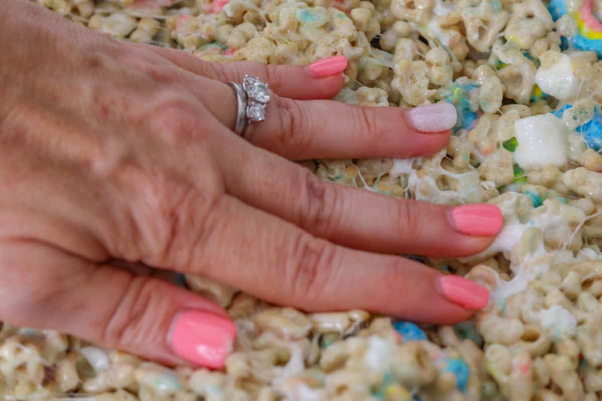Lucky Charm Krispie Treats | thewendthousekitchen.com Pressing down krispie treats with hand.