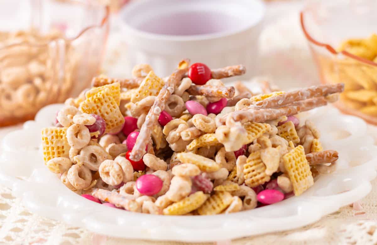 Valentine Bait Snack Mix on a white plate with cereal in bowls in the background.
