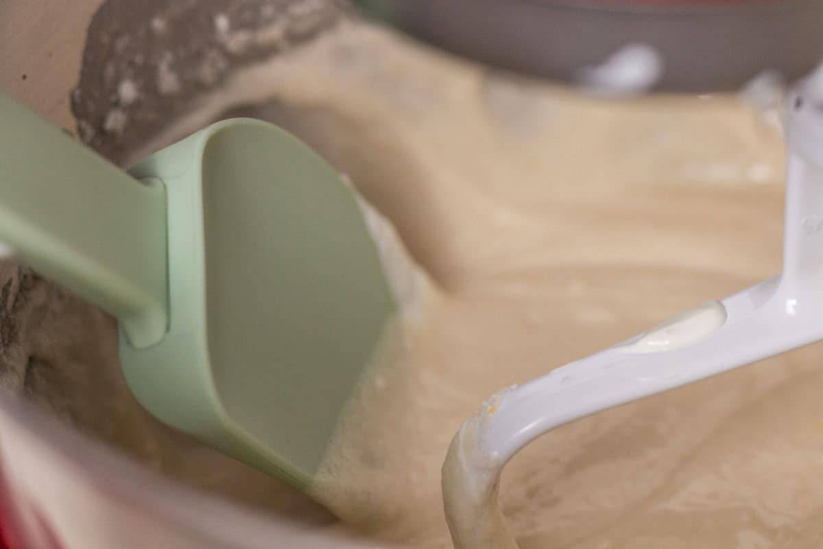 White Almond Sour Cream Cake | thewendthousekitchen.com White almond sour cream cake batter in the bowl of a stand mixer with a green silicone spatula.
