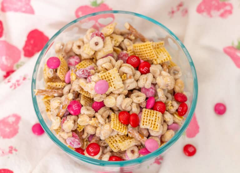 Valentine snack mix in a glass bowl with a pink, red and white dish towel underneath.