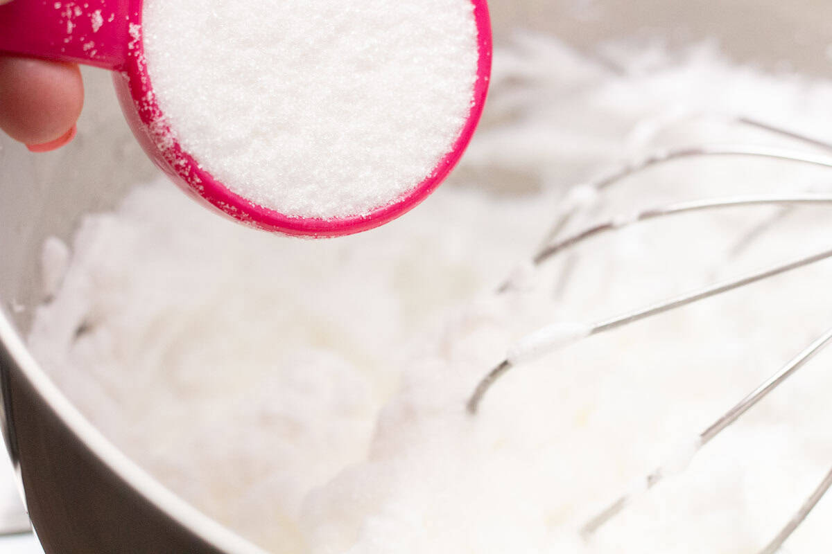 How To Make Italian Meringue Buttercream | thewendthousekitchen.com Pouring sugar over meringue in the bowl of a stand mixer.