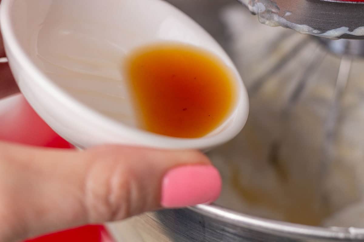 How To Make Italian Meringue Buttercream | thewendthousekitchen.com Pouring vanilla extract into the Italian meringue buttercream in the bowl of a stand mixer.