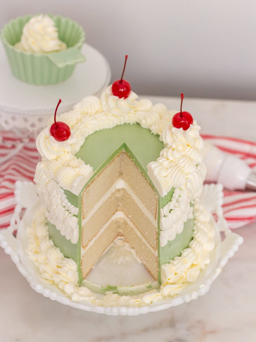 White Almond Sour Cream Cake | thewendthousekitchen.com White almond sour cream cake with a large slice cut out of it on a white plate with a red and white dish towel in the background.