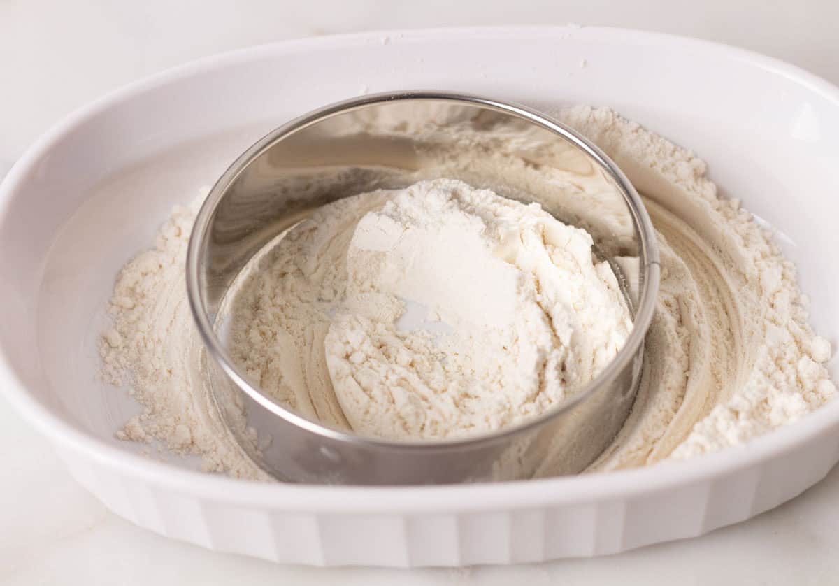 Sourdough Discard English Muffin Recipe | thewendthousekitchen.com Dipping cutter into flour in a white dish.