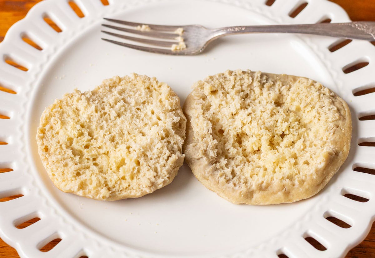 Sourdough Discard English Muffin Recipe | thewendthousekitchen.com An English muffin cut open on a white plate with a fork next to it.