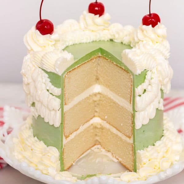 A green and white buttercream cake with cherries on top and a large slice cut out.