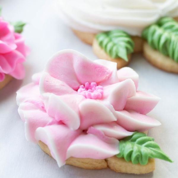 A sugar cookie decorated with a pink royal icing flower with a green leaf.