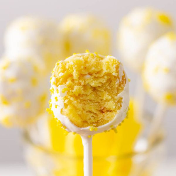 Lemon cake pop with a bite take out on a white stick.