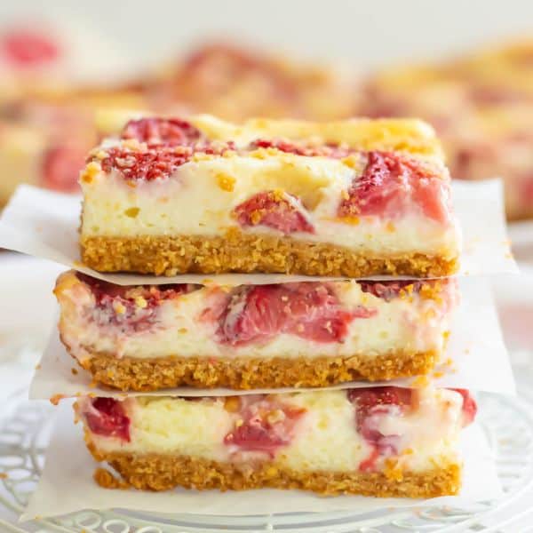 Strawberry Cheesecake Bars stacked between parchment paper on a white cake grid.