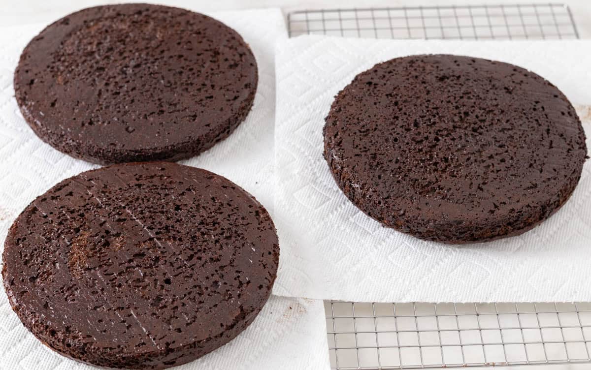 Chocolate Mint Cake with Mint Cream Cheese Frosting | thewendthousekitchen.com Three round chocolate cakes cooling on paper towels on a cooling grid.