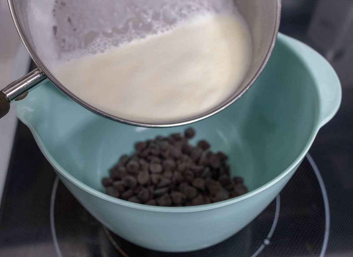 Chocolate Mint Cake with Mint Cream Cheese Frosting | thewendthousekitchen.com Pouring simmered heaving whipping cream into a medium aqua mixing bowl with chocolate chips.