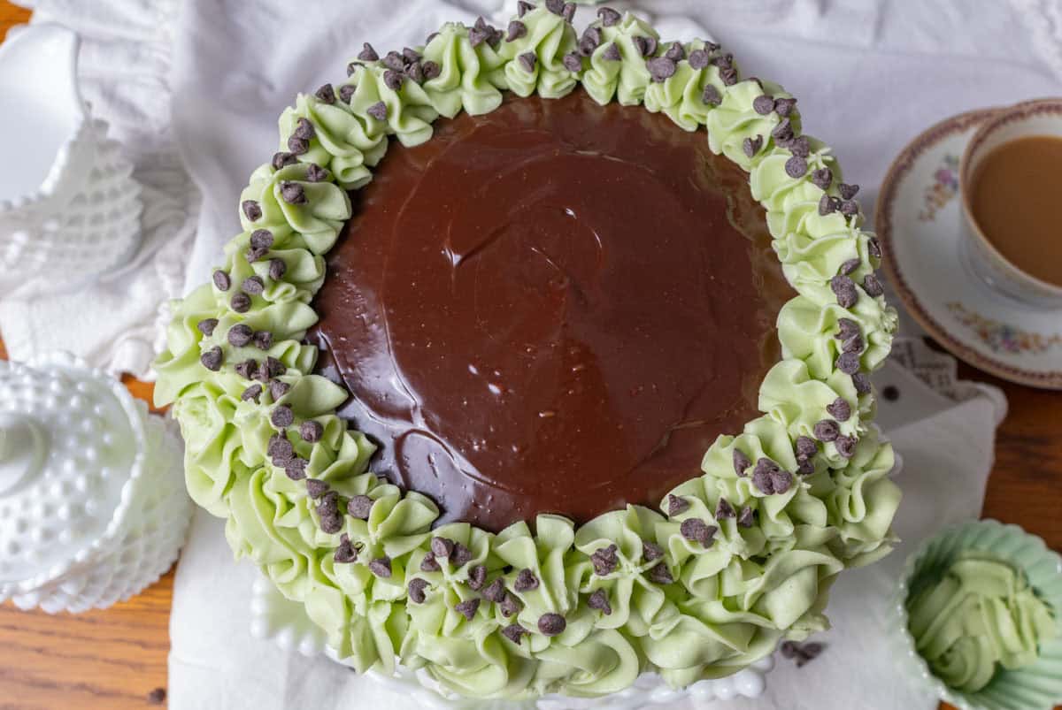 Chocolate Mint Cake with Mint Cream Cheese Frosting | thewendthousekitchen.com Top view of chocolate mint cake with green cream cheese frosting and ganache on the top. Coffee in the background and creamer and sugar bowl.