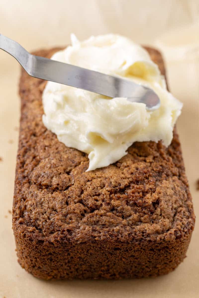 Carrot Cake Loaf Cake | thewendthousekitchen.com Spreading cream cheese frosting over the top of the carrot loaf cake with an offset icing spatula.
