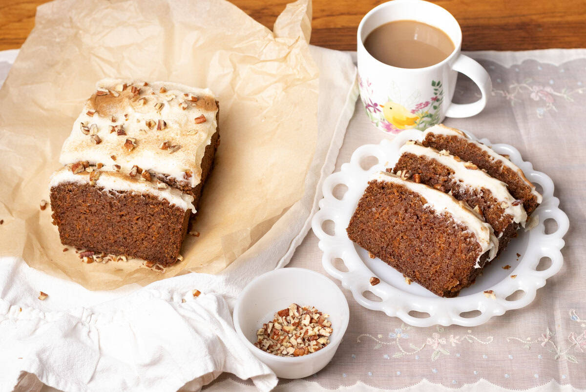 Carrot Cake Loaf Cake | thewendthousekitchen.com Carrot cake loaf cake sliced on a piece of brown parchment, then on the right, three pieces on a white plate. Cup of coffee in the background and a small bowl of chopped pecans in the front.