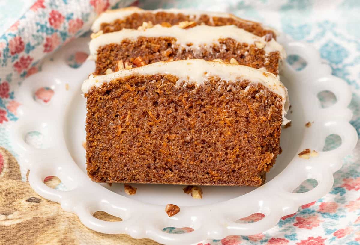 Carrot Cake Loaf Cake | thewendthousekitchen.com Carrot cake loaf cake on a white plate with a red and aqua dish towel in the background.