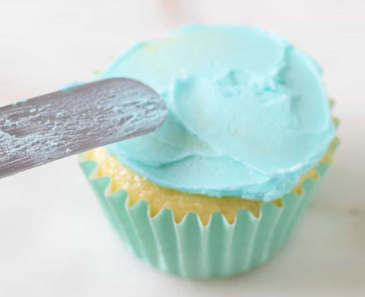 Bunny Cupcakes for Easter (Bunny Butt Cupcakes) | thewendthousekitchen.com Lightly frosting a cupcake with light turquoise frosting with an offset spatula.