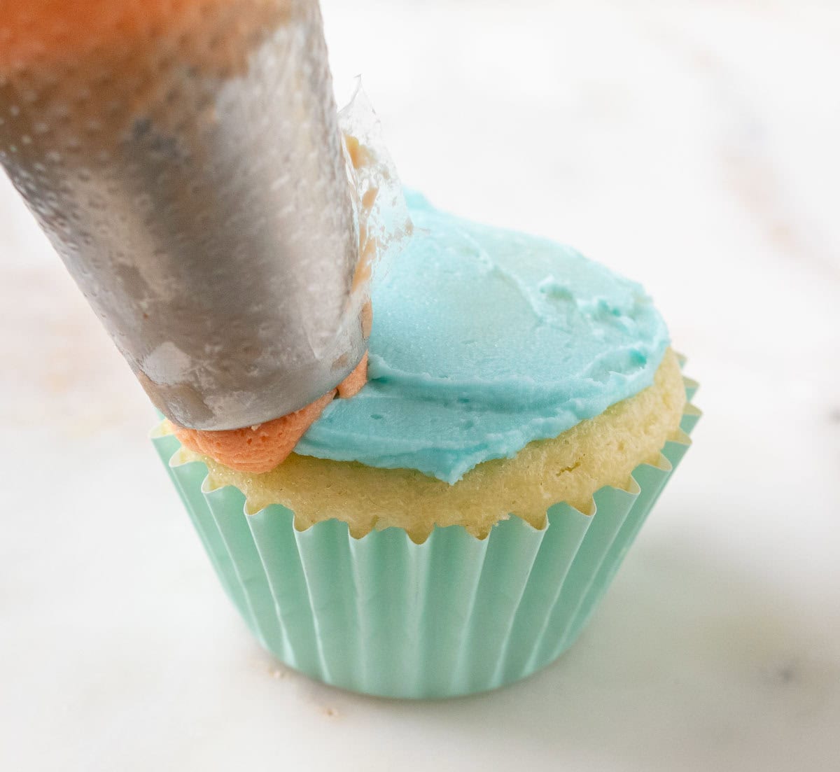 Bunny Cupcakes for Easter (Bunny Butt Cupcakes) | thewendthousekitchen.com A piping bag with orange frosting held over a froated cupcake.
