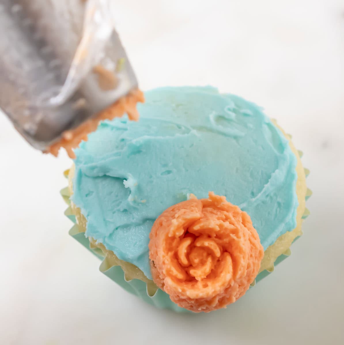 Bunny Cupcakes for Easter (Bunny Butt Cupcakes) | thewendthousekitchen.com An orange buttercream flower just piped onto a frosted cupcake with the piping bag held above.
