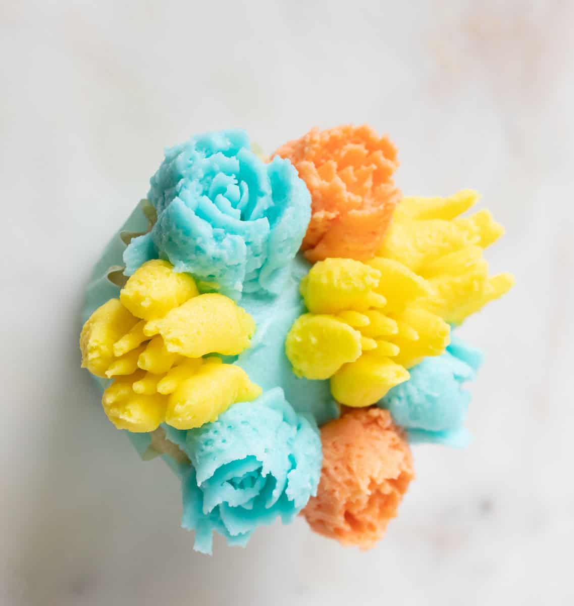 Bunny Cupcakes for Easter (Bunny Butt Cupcakes) | thewendthousekitchen.com Buttercream flowers in light turquoise, yellow and orange around a cupcake.