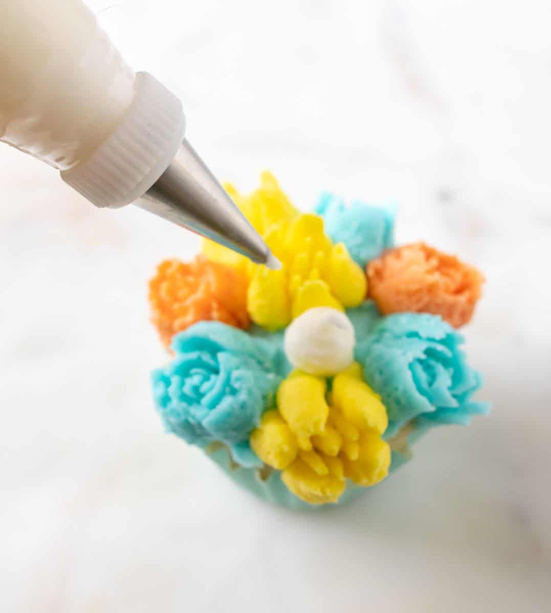 Bunny Cupcakes for Easter (Bunny Butt Cupcakes) | thewendthousekitchen.com Adding a large white buttercream dot to the middle of a cupcake decorated with turquoise, yellow and orange flowers.