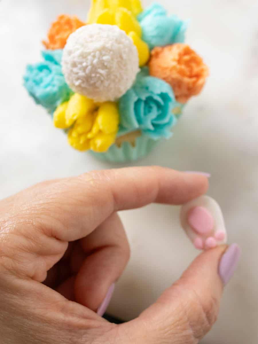 Bunny Cupcakes for Easter (Bunny Butt Cupcakes) | thewendthousekitchen.com Holding a bunny paw over a cupcake decorated with butercream flowers and a Raffaello candy.