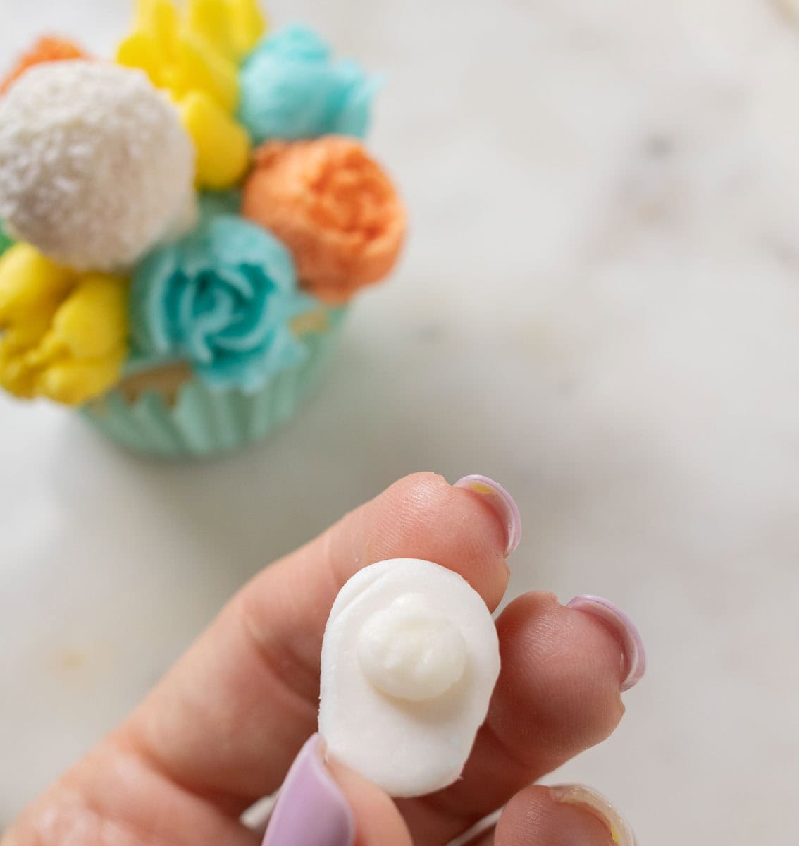 Bunny Cupcakes for Easter (Bunny Butt Cupcakes) | thewendthousekitchen.com A white dot of buttercream on the back of a fondant bunny paw with a decorated cupcake in the back.