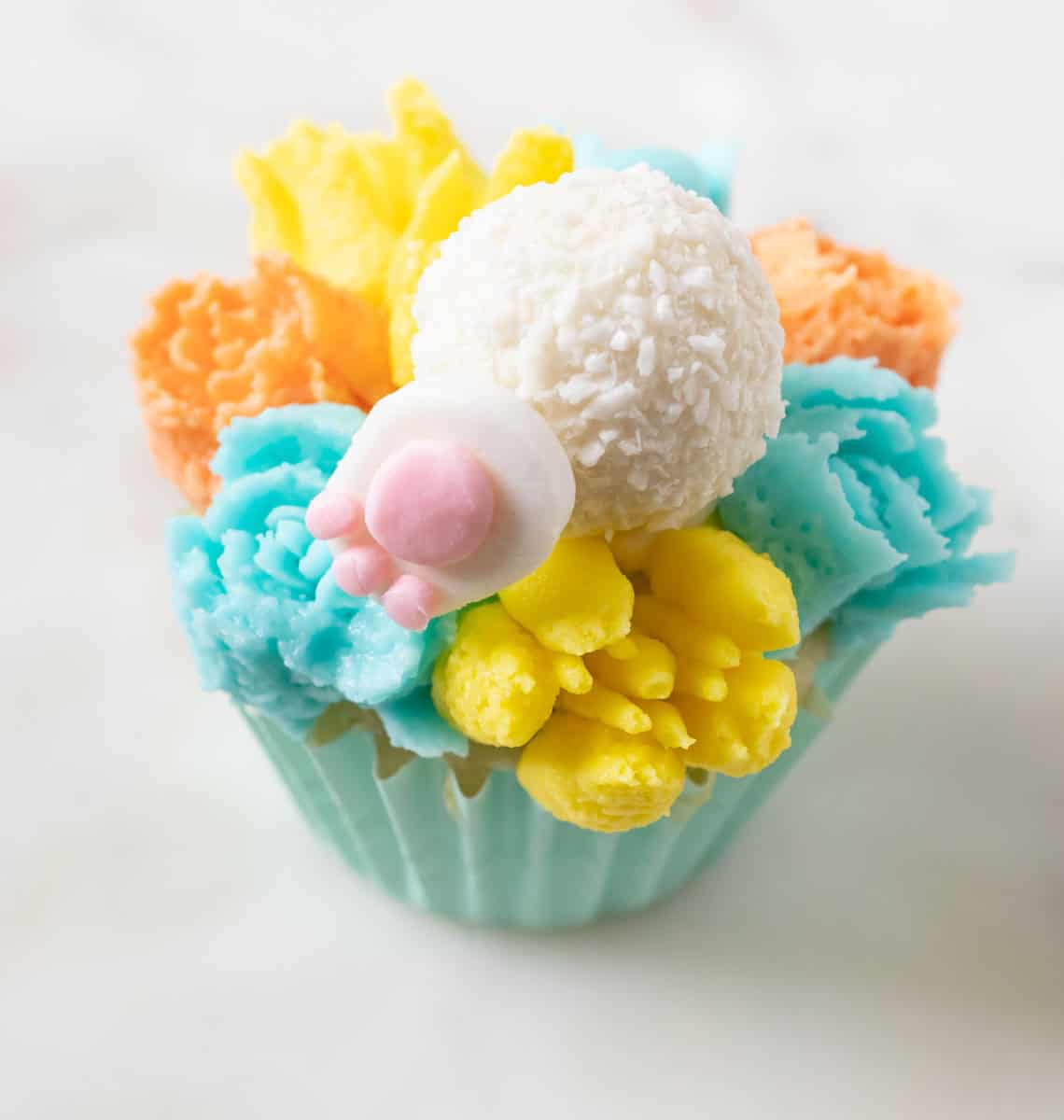 Bunny Cupcakes for Easter (Bunny Butt Cupcakes) | thewendthousekitchen.com A bunny paw on one side of a Raffello candy that is on a cupcake decorated with buttercream flowers.