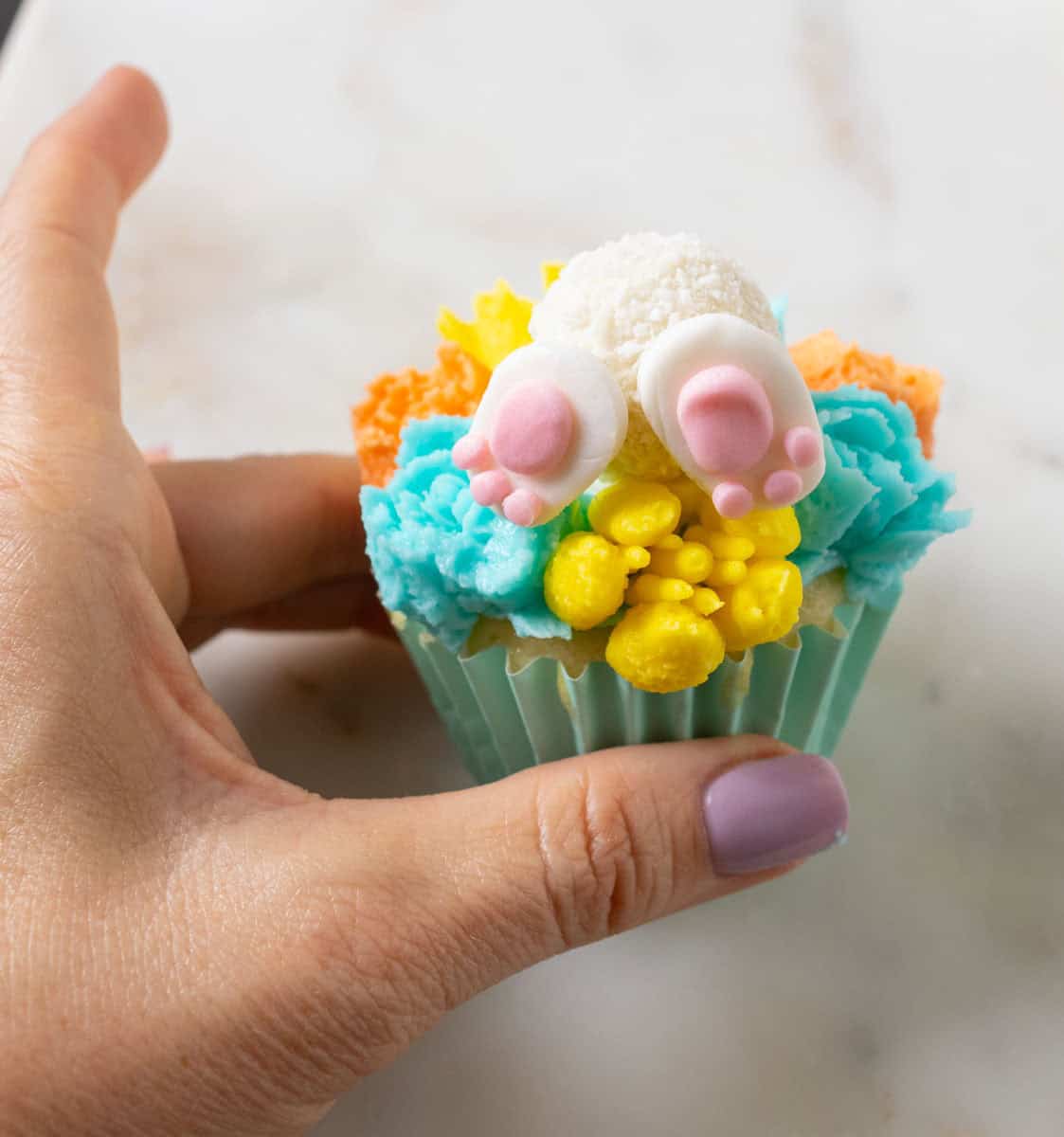 Bunny Cupcakes for Easter (Bunny Butt Cupcakes) | thewendthousekitchen.com Two bunny paws on a Raffello candy that is on a cupcake decorated with buttercream flowers.