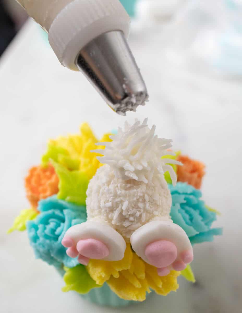 Bunny Cupcakes for Easter (Bunny Butt Cupcakes) | thewendthousekitchen.com A piping bag with tip #233 held over a mini marshmallow with white buttercream frosting.