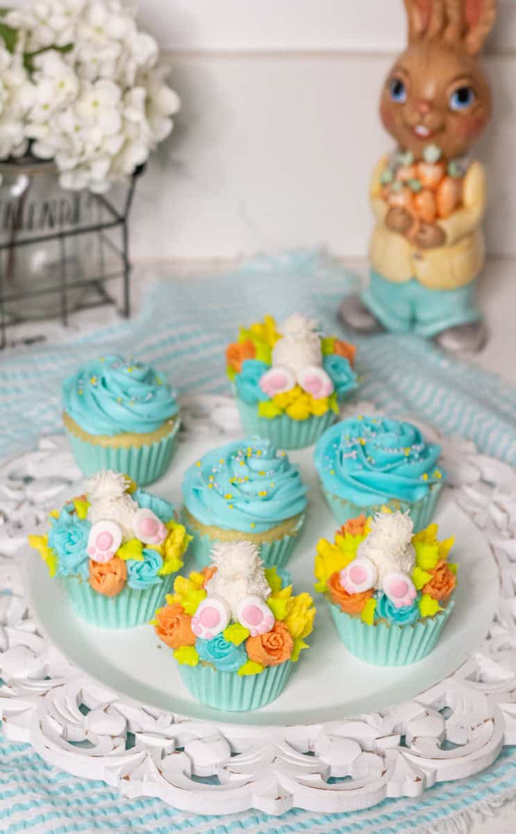 Bunny Cupcakes for Easter (Bunny Butt Cupcakes) | thewendthousekitchen.com Bunny butt cupcakes decorated with orange, turquoise and yelllow flowers in a light turquoise cupcake liner with other cupcakes decorated with a turquoise swirl on a white tray.