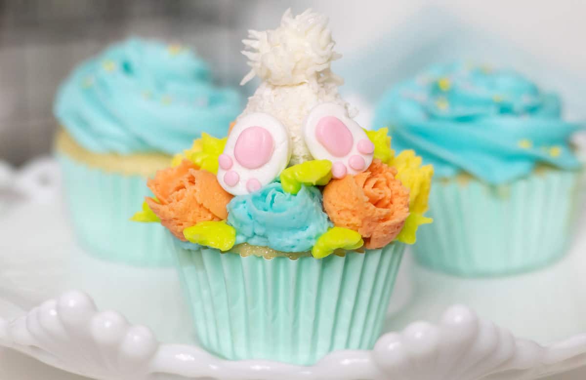 Bunny butt cupcake with orange, turquoise and yellow flowers in a light turquoise cupcake liner with other cupcakes in the background.
