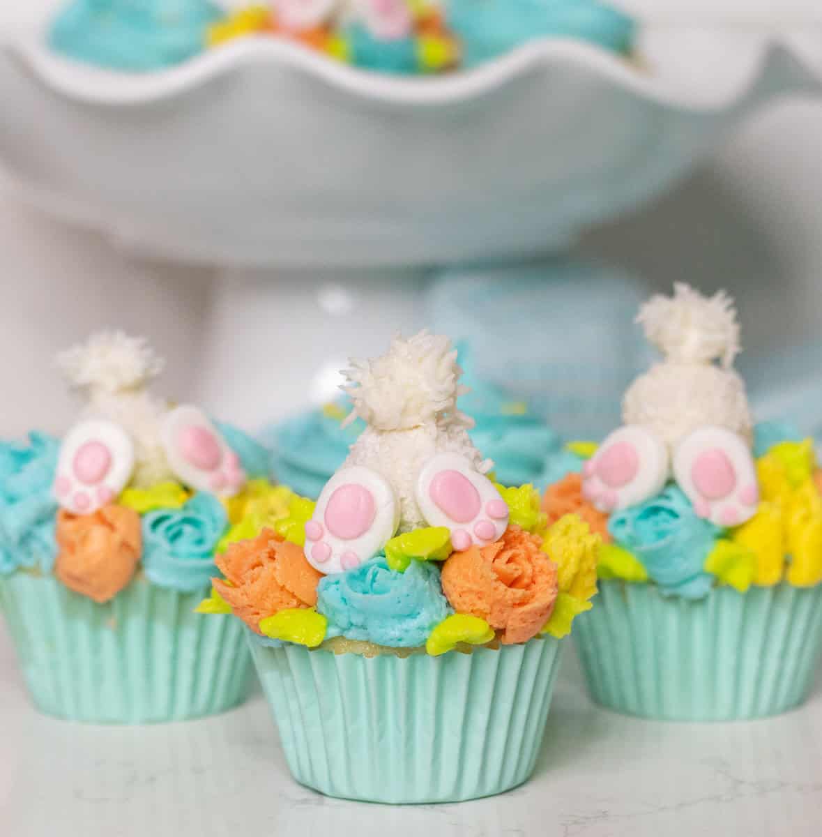 Bunny butt cupcakes with more cupcakes on a cake stand in the background.