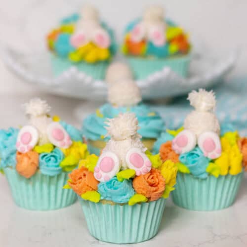 Three bunny butt cupcakes and some in the background on a white cake plate.