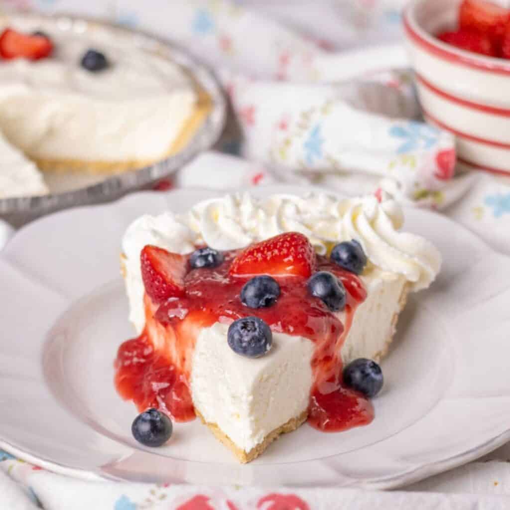 Piece of no bake cheesecake on a white plate with strawberry sauce and berries.