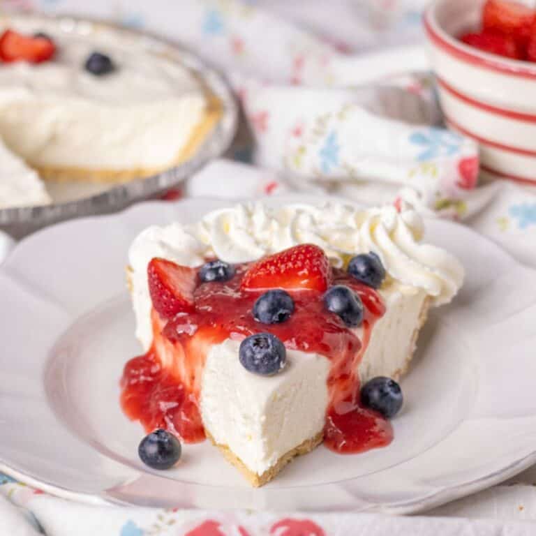 Piece of no bake cheesecake on a white plate with strawberry sauce and berries.