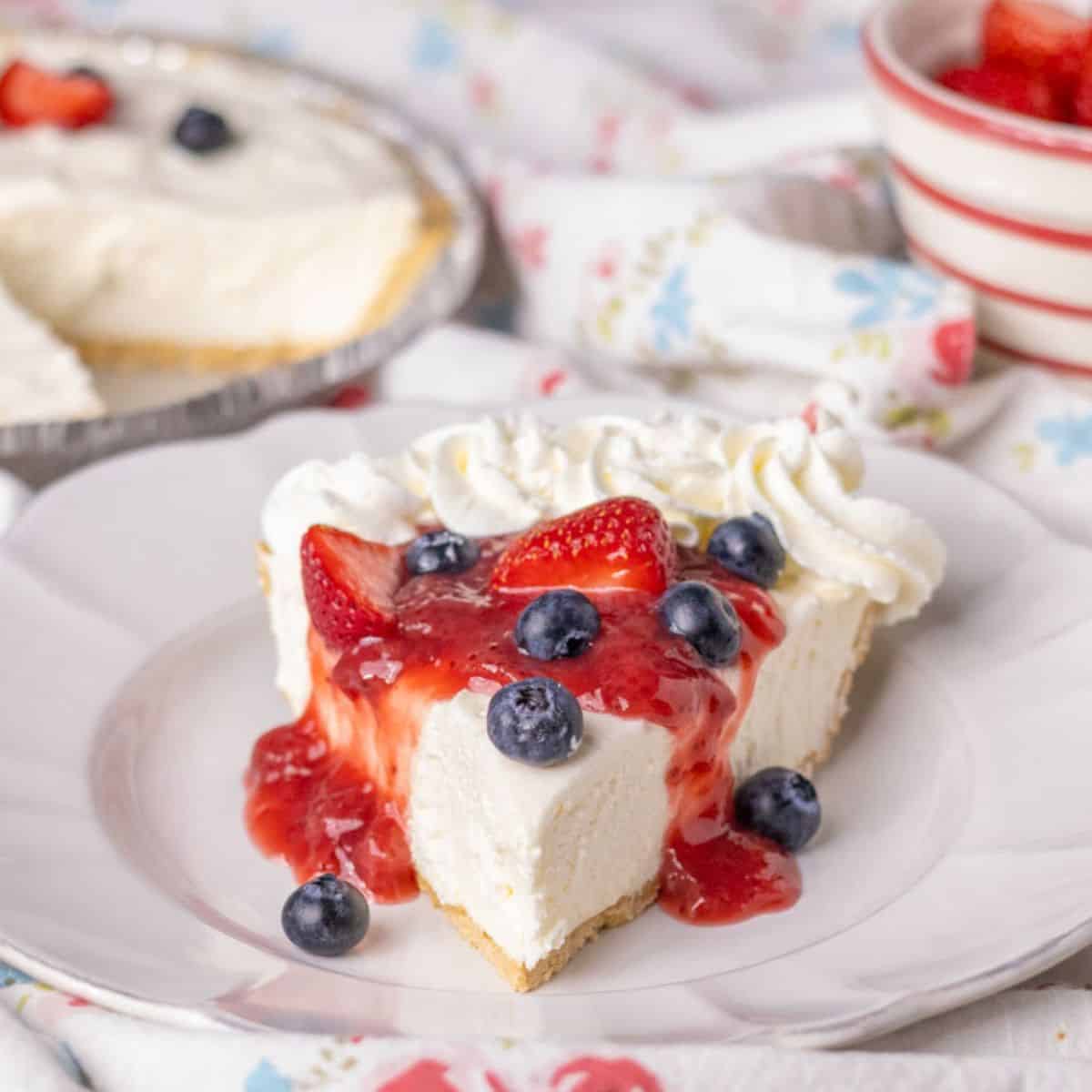 Piece of no bake cheesecake on a white plate with strawberry sauce and berries.