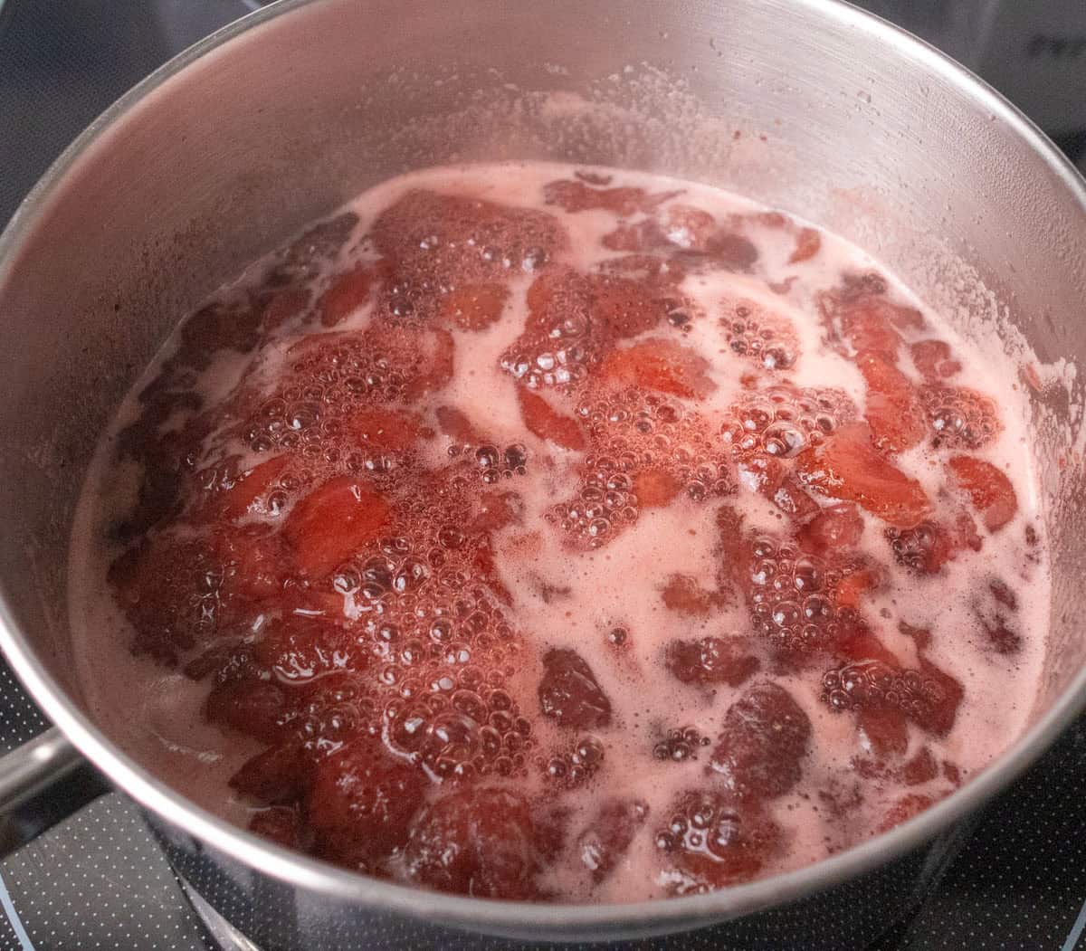 How To Make Strawberry Sauce | thewendthousekitchen.com Strawberries, water and sugar simmering in a medium saucepan and the strawberries starting to break down.