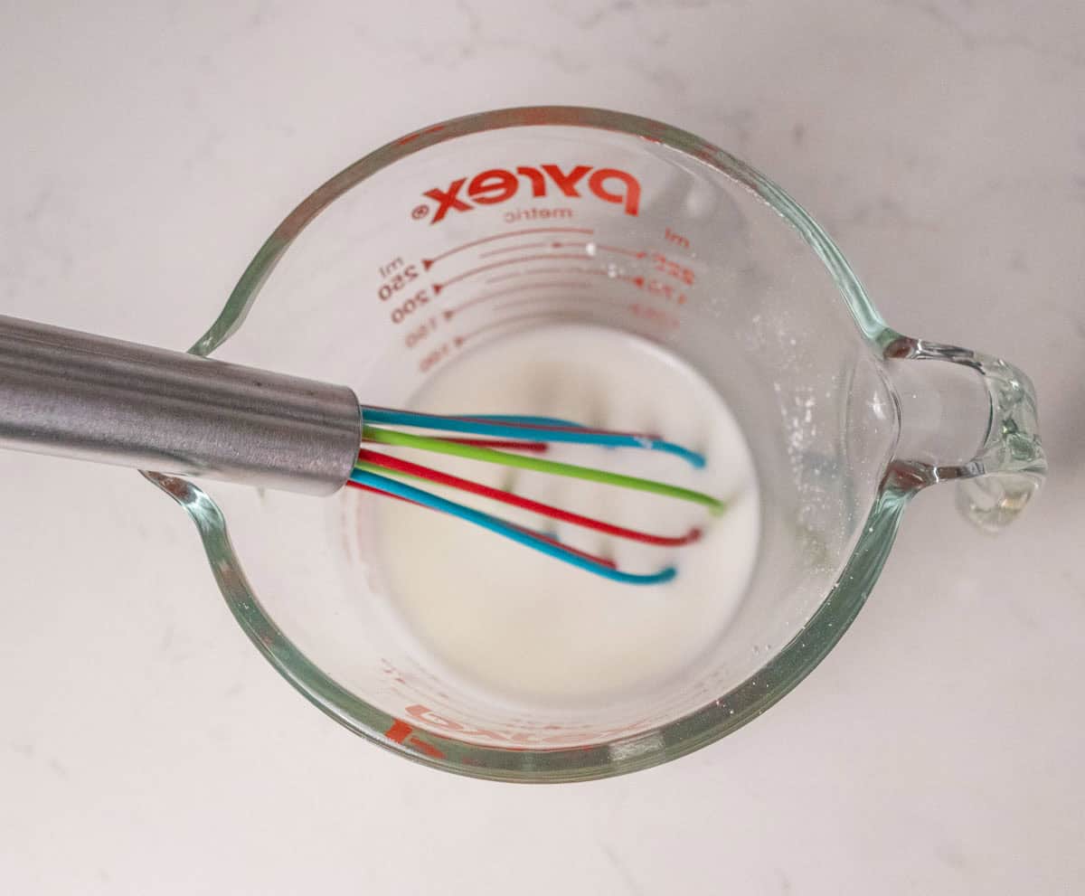 How To Make Strawberry Sauce | thewendthousekitchen.com Stirring water and cornstarch together inside a glass measuring cup with a small whisk.