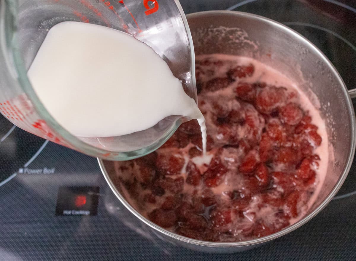 How To Make Strawberry Sauce | thewendthousekitchen.com Pouring cornstarch slurry into the saucepan with the cooked strawberries, sugar and water.