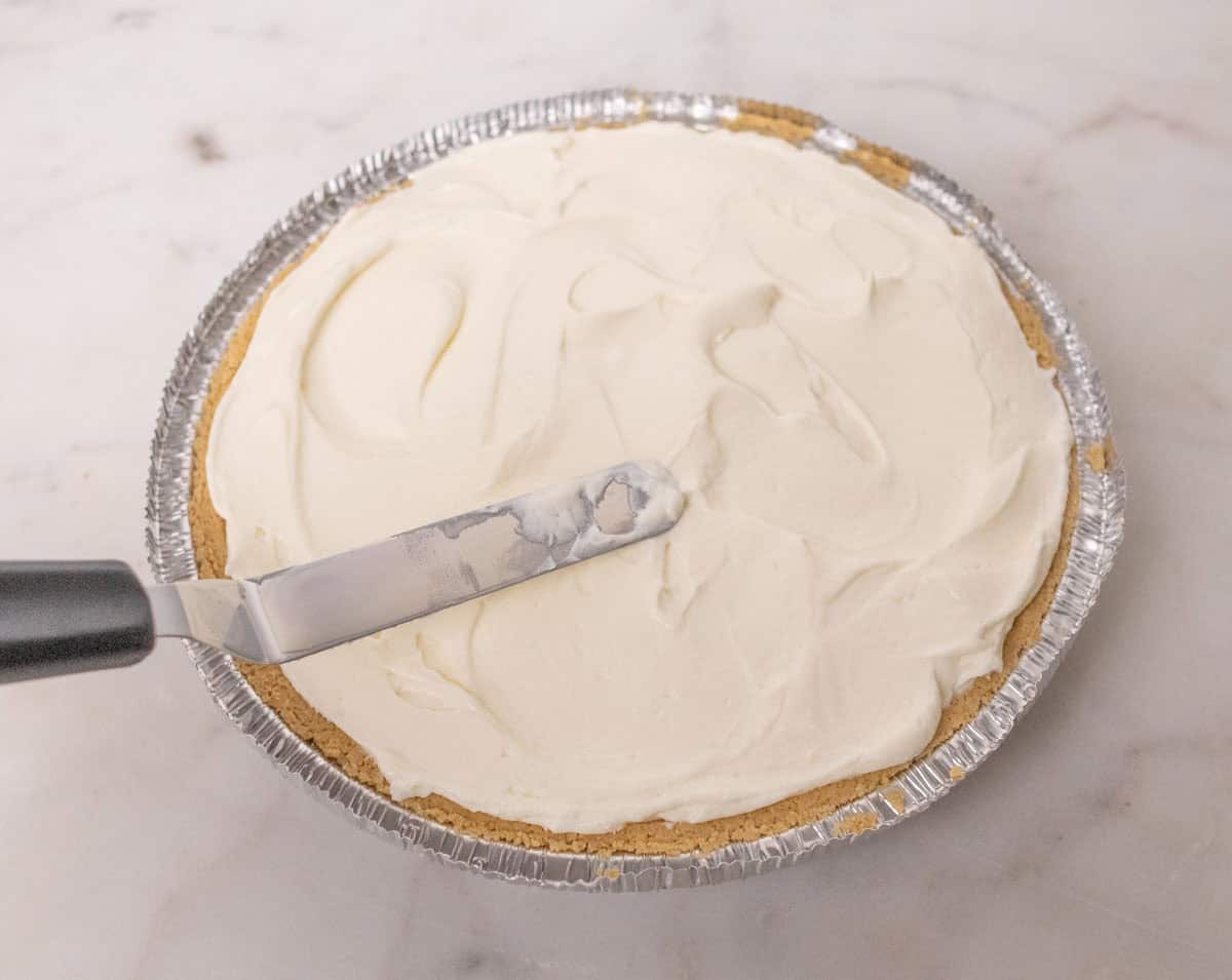 3 Ingredient No Bake Cheesecake | thewendthousekitchen.com Spreading cheesecake filling evenly inside of a premade graham cracker pie shell.