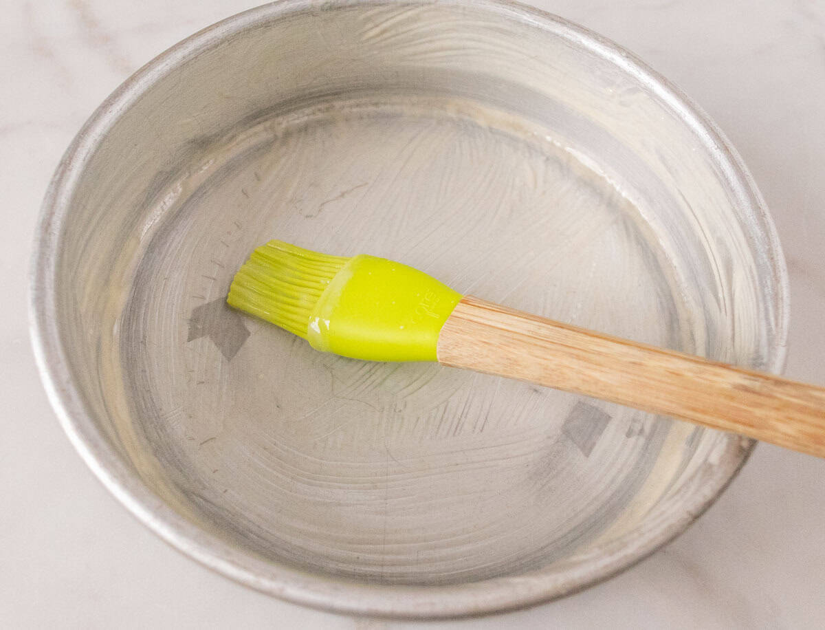 Strawberry Crunch Cake | thewendthousekitchen.com Greasing a round cake pan with cake release using a green silicone brush.