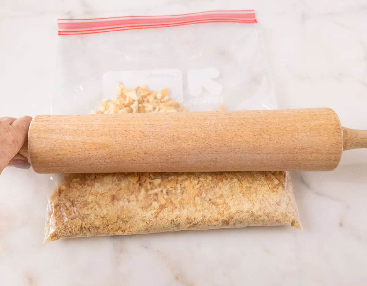 Strawberry Crunch Cake | thewendthousekitchen.com Crushing vanilla wafers in a sealed storage bag with a rolling pin.