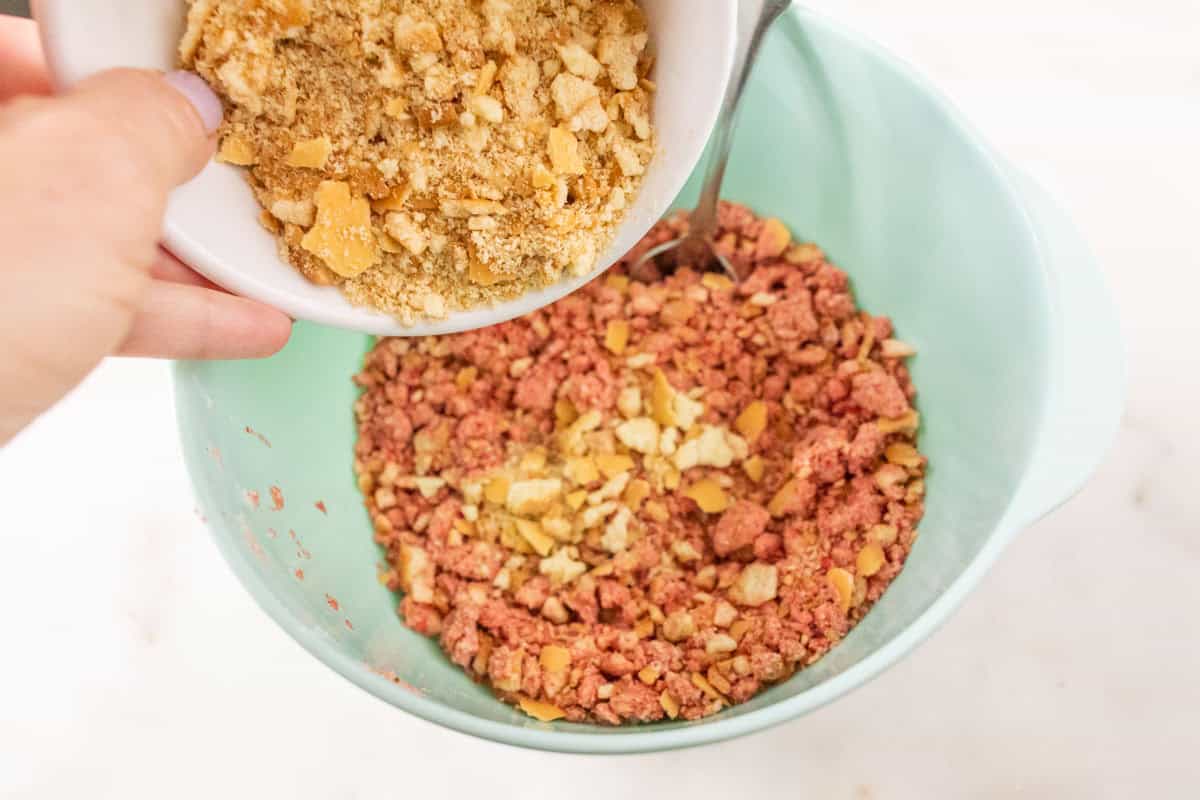 Strawberry Crunch Cake | thewendthousekitchen.com Adding additional vanilla wafers to strawberry crunchies in a light turquoise mixing bowl.