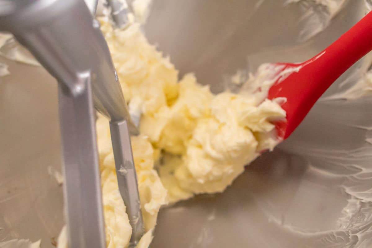 Strawberry Crunch Cake | thewendthousekitchen.com Beating butter with a paddle attachment and scraping down the bowl with a red silicone spatula.