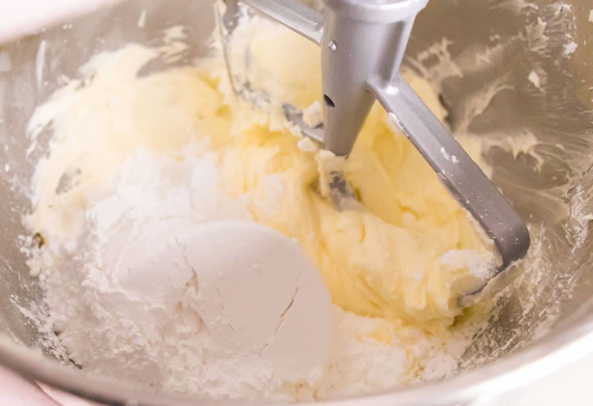 Strawberry Crunch Cake | thewendthousekitchen.com Adding powdered sugar to whipped butter in the bowl of a stand mixer with a paddle attachment.